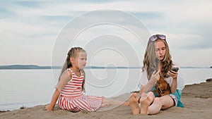 Two teenage are sitting on a sandy beach, on the Internet in phone.