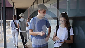 Two teenage students discussing while standing with workbooks near college building on autumn day