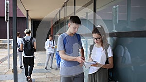 Two teenage students discussing while standing with workbooks near college building on autumn day