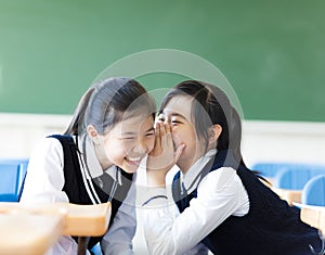 Two teenager girls gossiping in classroom