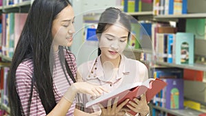 Two teenager girls read a book at book shelf in background .