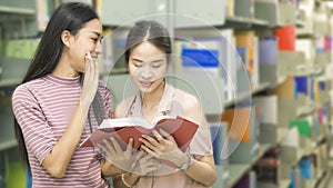 Two teenager girls read a book at book shelf in background .