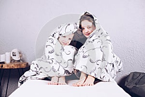 Two teenagers are laughing wrapped in a blanket. A girl and a boy are sitting on the bed hugging each other. Happy