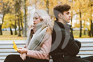 Two teenagers in love in a quarrel. A brunette boy and a blonde girl are sitting on opposite ends of the benches, their backs to