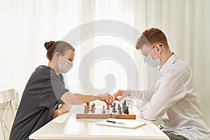 Two teenagers play chess during quarantine due to coronavirus pandemic. Boy and girl play Board games