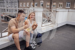 Two teenagers are sitting on the parapet on the roof of the house and eating Asian food photo