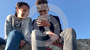 Two teenagers sitting in the street and watching funny videos on the phone.