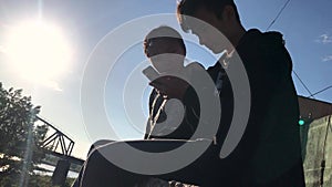 Two teenagers sitting in the street and watching funny videos on the phone.