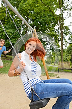 Two teenagers sitting swing in park playground