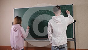 Two teenagers stand near the blackboard and solve a mathematical problem.
