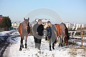 Two teenagers and two horses walking in the snow