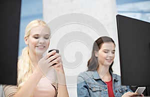 Two teens with smartphones in computer class