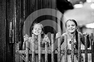 Two ten-year-old girls posing near a rustic wooden fence. Black and white photography.