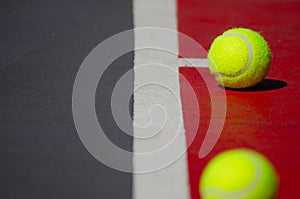 two tennis balls resting on a tennis court that appears to have been painted red