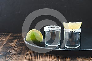Two Tequila shots with lime slices and salt on wooden table/Tequila shots and lime slice on wooden table with Copy cpace on dark