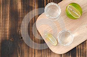 Two Tequila shots with lime slices and salt on wooden table/Tequila shots and lime slice on wooden table with Copy cpace. Top view