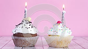 Two testy sweet cup cakes with cream and burning candles on the table