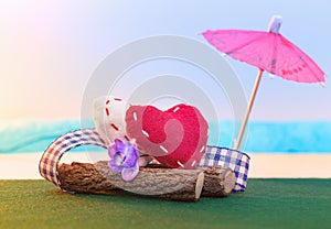 Two textile hearts sit on a log on the seashore