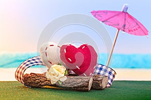 Two textile hearts sit on a log on the seashore