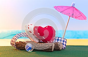 Two textile hearts sit on a log on the seashore