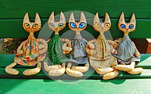 Two textile toy cats with big expressive eyes are sitting on a green bench on a sunny summer day and holding their paws photo