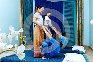 Two thai masseuses synchronously doing thai massage.