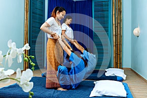 Two thai masseuses synchronously doing thai massage.