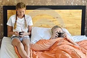 The two of them play on the phone in the bed. Children`s mobile addiction. Teenagers are surfing the internet