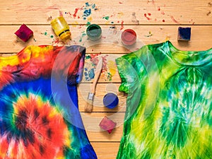 Two tie dye t-shirts and a fabric painting kit on a wooden table. Flat lay.