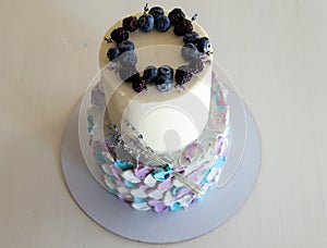 Two-tier cream cake in blue-gray-lilac colors, decorated with blueberries and sprigs of lavender on black stand. Wedding