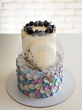 Two-tier cream cake in blue-gray-lilac colors, decorated with blueberries and sprigs of lavender on black stand. Wedding