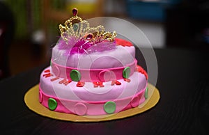 Two-tier fondant cake design with a tiara on top, decorated with icing flowers. Delicious pink-red color-themed round cake on