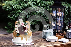 Two tiered white and gold wedding cake with red and pink roses and ruscus leaves on a wooden vintage cart