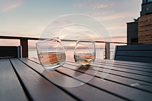Two tilted tumbler glasses of whiskey on deck table