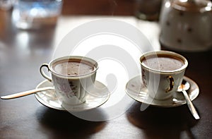 Two tiny coffee cup with hot milk coffee and teaspoons