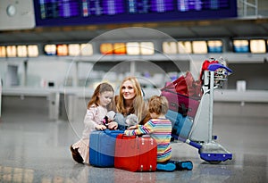 Two tired little kids, boy and girl, siblings and mother at the airport. Children, family traveling, going on vacation