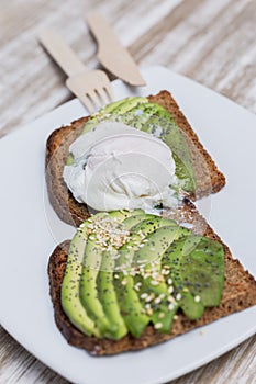 Two toasts with avocado, sesame and egg on a wooden table