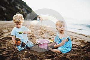 Two toddler children playing on sand beach on summer holiday.