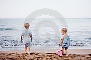 Two toddler children playing on sand beach on summer holiday.