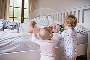 Two toddler children with smartphone and their father on bed in the bedroom.