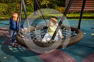 Two toddlers a boy and a girl play cheerfully and swing on a swing hammock on a playground in the autumn park
