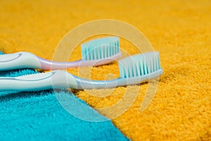 Two toothbrushes lie side by side on yellow and blue towels