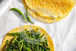 two tortillas filled with green peas and beans on top of paper