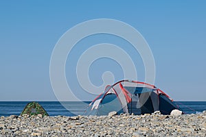 Two tourist tents on a pebble sea shore in the morning