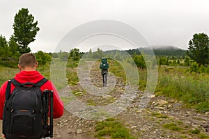 Two tourists with backpacks go on the road covered with stones,