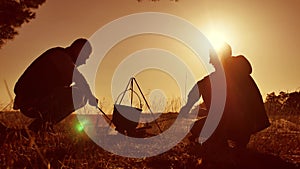Two tourists beer are sitting by bonfire lifestyle bonnet party in nature camping silhouette sunlight sunset. two men