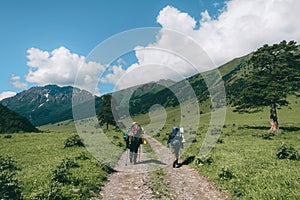 Two tourists going trekking by the green mountain valley