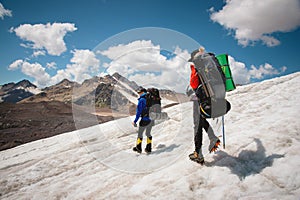 Two tourists, a man and a woman with backpacks and crampons on their feet walk along the glacier against the background