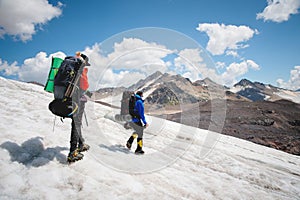 Two tourists, a man and a woman with backpacks and crampons on their feet walk along the glacier against the background