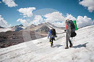 Two tourists, a man and a woman with backpacks and crampons on their feet walk along the glacier against the background